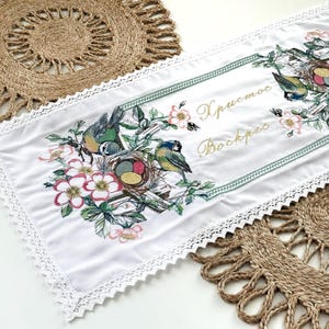 May include: White table runner with embroidered birds, nests, and floral designs. The runner has a delicate lace trim and the text "Христос Воскрес" in gold script. The design includes birds with blue, green, and yellow feathers.