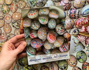 May include: A close-up of intricately painted Easter eggs, with vibrant colours and intricate designs. The eggs are arranged in a basket, with a sign reading "Авторські писанки Зої Стащук".