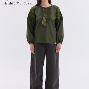 May include: An olive green blouse with embroidered details and a tassel, paired with dark gray wide-leg pants. The model is wearing size S. Bust 33 inches, waist 24.5 inches, hips 36 inches, and height 5'7 inches.