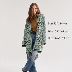 May include: A light mint green open-front cardigan featuring a dark green geometric pattern. The garment is labeled as one size, fitting US 8-16, and is composed of 50% wool and 50% acrylic. Text on the image includes model measurements and material.