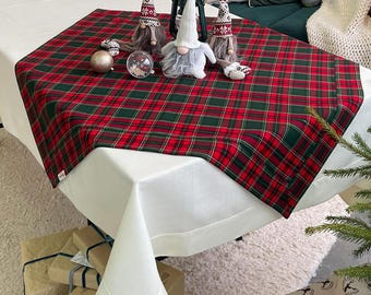 May include: A festive holiday table setting featuring a red and green plaid table runner. The table is decorated with gnome figurines, ornaments, and a lantern. A white tablecloth and wrapped gifts complete the scene.