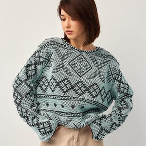 Pode incluir: Um suéter azul claro com um padrão geométrico preto. O suéter tem gola redonda e mangas compridas.
