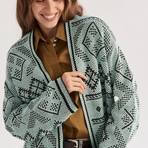 May include: A mint green and black open-front cardigan featuring a repeating geometric pattern throughout the knit fabric. The garment has long sleeves, a straight hem, and a solid black trim along the front opening and the sleeve cuffs.