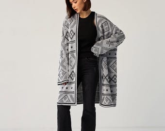 May include: A long, white cardigan with a black geometric pattern. The cardigan is open and worn over a black tank top and black jeans.