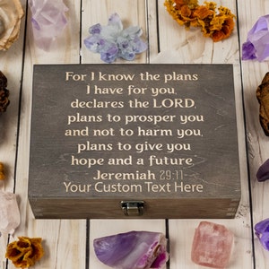 May include: A wooden box with a hinged lid and a metal latch. The box has a quote from Jeremiah 29:11 engraved on the top: "For I know the plans I have for you, declares the LORD, plans to prosper you and not to harm you, plans to give you hope and a future." The box also has the text "Your Custom Text Here" engraved on the bottom.