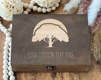 May include: A wooden box with a hinged lid and a latch closure. The box is decorated with a laser-engraved design of a tree with a sun behind it. The text "YOUR CUSTOM TEXT HERE" is engraved below the tree.