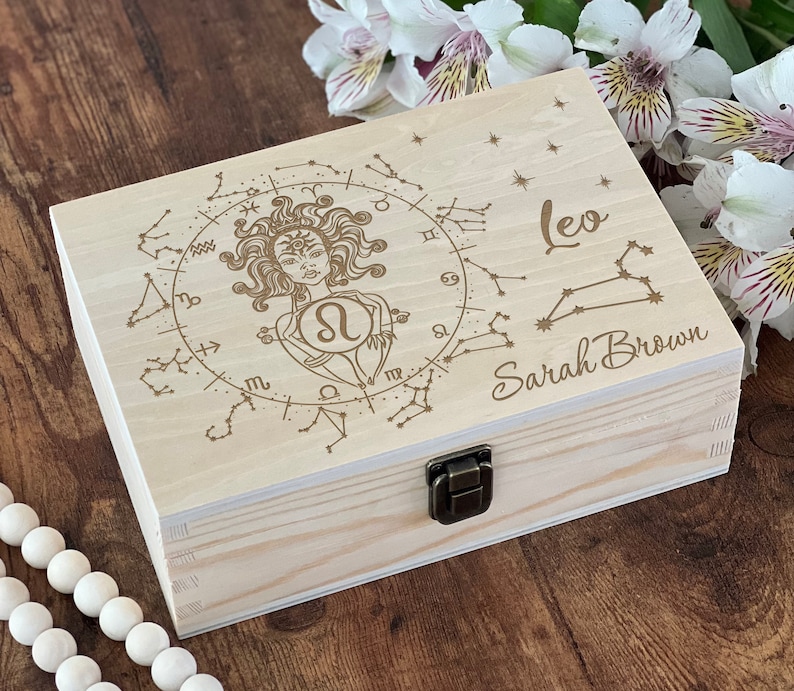May include: A wooden box with a hinged lid and a latch. The box is engraved with a zodiac sign, the constellation Leo, and the name "Sarah Brown".