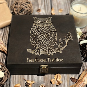 Peut inclure: Une boîte en bois noire avec un motif de hibou doré et le texte "Your Custom Text Here". La boîte a un couvercle à charnières et un loquet en métal.