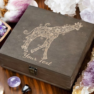 May include: A dark brown wooden box with a hinged lid and a latch. The box is decorated with a laser-engraved mandala-style giraffe design. The text "Your Text" is engraved below the giraffe.