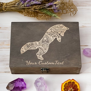 Pode incluir: Uma caixa de madeira castanho-escuro com uma tampa articulada e um fecho. A caixa é decorada com um desenho de uma raposa estilizada gravada a laser com padrões intrincados. O texto "Your Custom Text" está gravado abaixo do desenho da raposa.