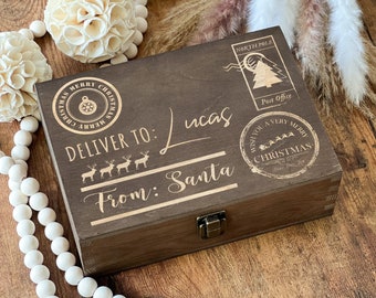 May include: A brown wooden box with a hinged lid and a metal clasp. The box is decorated with a gold-coloured design that says "Deliver to: Lucas From: Santa". There are also several gold-coloured stamps on the box, including one that says "Wish you a very Merry Christmas".