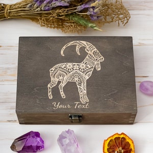 Peut inclure: Une boîte en bois brun foncé avec un couvercle à charnières et un fermoir en métal. La boîte présente un motif complexe de chèvre avec des motifs floraux. Le texte "Your Text" est gravé sur le devant de la boîte.