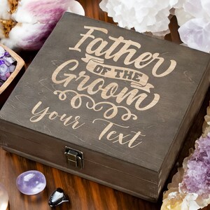 May include: A dark brown wooden box with a hinged lid and a brass latch. The box is engraved with the text "Father of the Groom" and "Your Text".