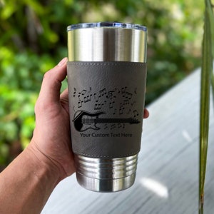 May include: A stainless steel tumbler with a gray leatherette wrap. The wrap features a black silhouette of an electric guitar with musical notes. The text "Your Custom Text Here" is printed on the wrap.