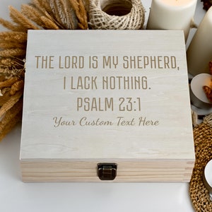 May include: A wooden box with a hinged lid and a metal latch. The box is white and has the text "THE LORD IS MY SHEPHERD, I LACK NOTHING. PSALM 23:1 Your Custom Text Here" engraved on the top.