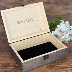 May include: A wooden box with a hinged lid and a metal latch. The box is open and the inside is lined with black velvet. The lid has the text "Your text" engraved on it.