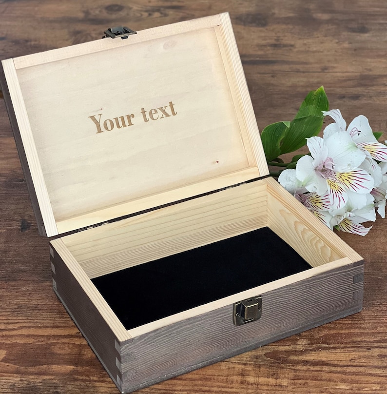 May include: A wooden box with a hinged lid and a metal latch. The box is open and the inside is lined with black velvet. The lid has the text "Your text" engraved on it.