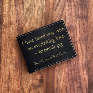 Peut inclure: Portefeuille en cuir noir avec inscription dorée. Le texte indique "I have loved you with an everlasting love. - Jeremiah 31:3" et "Your Custom Text Here".