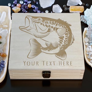 Könnte beinhalten: Eine Holzkiste mit einem Scharnierdeckel und einem Messingverschluss. Die Kiste ist mit einem gravierten Bild eines Barsches und dem Text "YOUR TEXT HERE" verziert.
