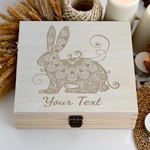 May include: A wooden box with a hinged lid and a latch. The box is decorated with an engraved design of a rabbit with intricate mandala patterns. The text "Your Text" is engraved below the rabbit.