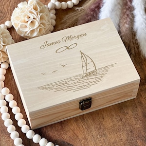 Könnte beinhalten: Eine Holzkiste mit einem Segelboot und einem Unendlichkeitszeichen, das in den Deckel graviert ist. Die Kiste ist mit dem Namen "James Morgan" personalisiert.