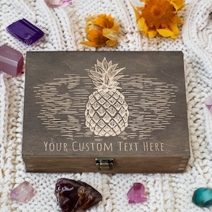 May include: A wooden box with a hinged lid and a brass latch. The box is decorated with an engraved image of a pineapple and the text "YOUR CUSTOM TEXT HERE".