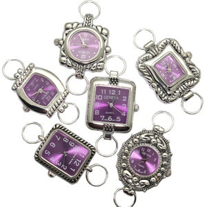 May include: Six silver-toned watch charms with purple faces. The watch faces have Roman numeral markings and the words "GENEVA" and "QUARTZ".