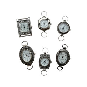 May include: Six silver-toned watch faces with black Roman numeral markings and rhinestone accents. The watches have a clasp closure and are designed to be worn on a chain or necklace.