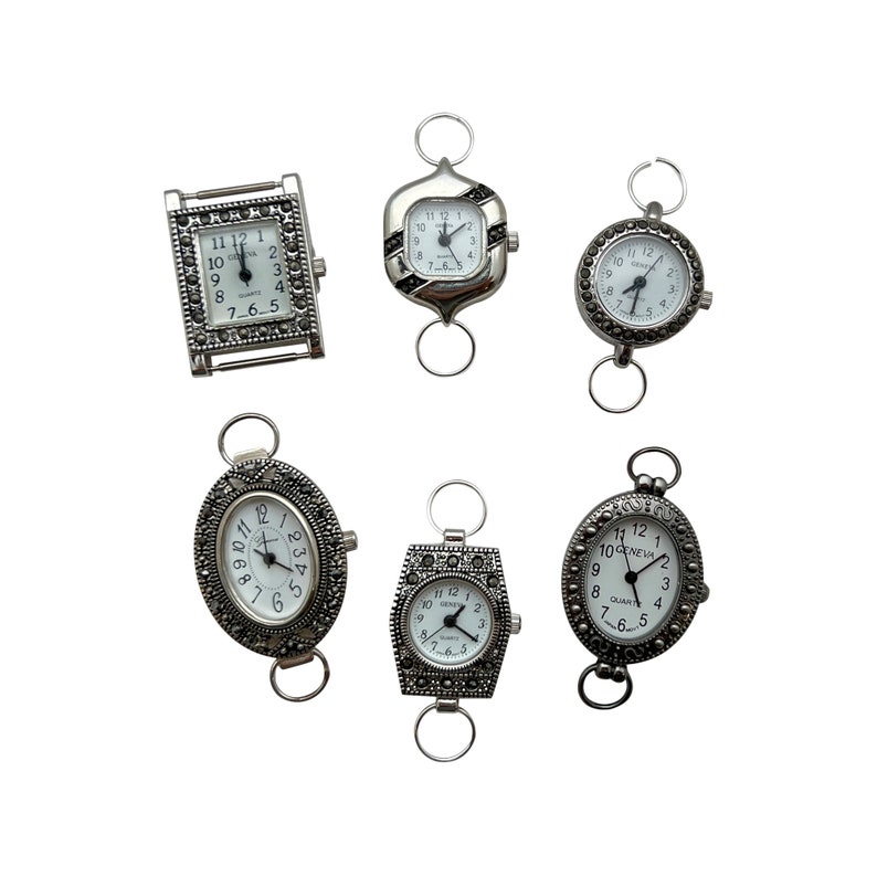 May include: Six silver-toned watch faces with black Roman numeral markings and rhinestone accents. The watches have a clasp closure and are designed to be worn on a chain or necklace.