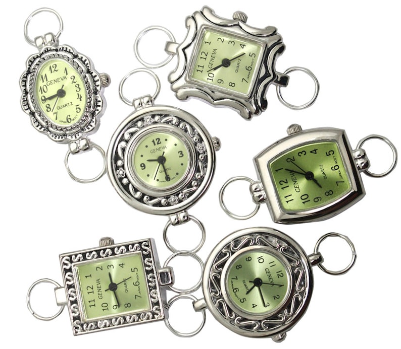 May include: Six silver-tone pocket watches with green faces and black hands. The watches are connected by silver-tone chains. Each watch has a different design around the face.