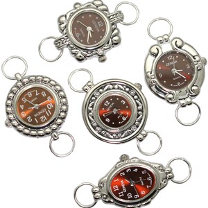 May include: Five silver-toned watch charms with different designs. Each charm features a round watch face with a brown face and black hands. The watch faces have the text "GENEVA" and "QUARTZ" printed on them.