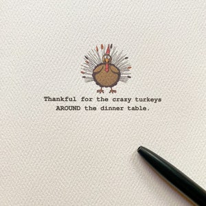 May include: A Thanksgiving greeting card with a cartoon turkey illustration. The turkey is brown with a red wattle and a festive headdress. The text reads, "Thankful for the crazy turkeys around the dinner table."