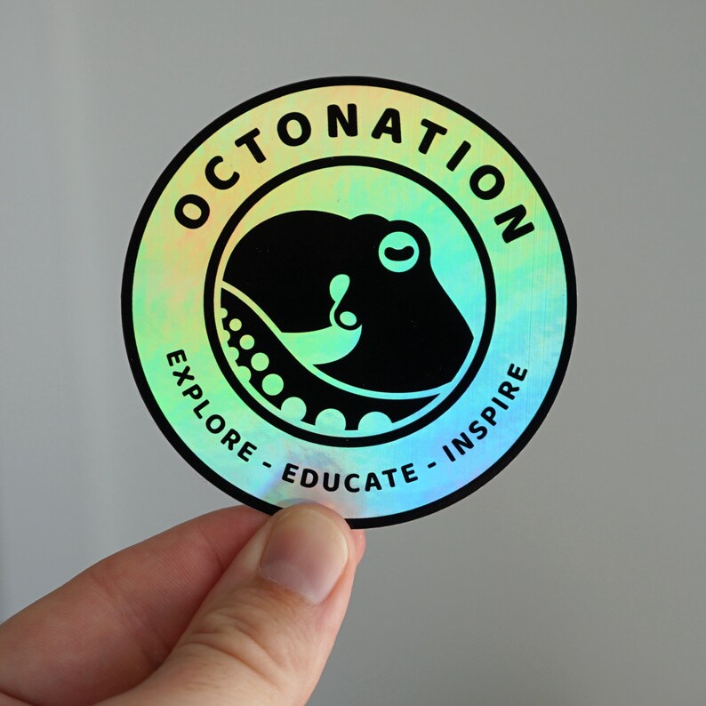 May include: Circular sticker with a holographic finish featuring a black octopus design inside a black circle. The text "OCTONATION" arches across the top, with "EXPLORE - EDUCATE - INSPIRE" along the bottom edge.
