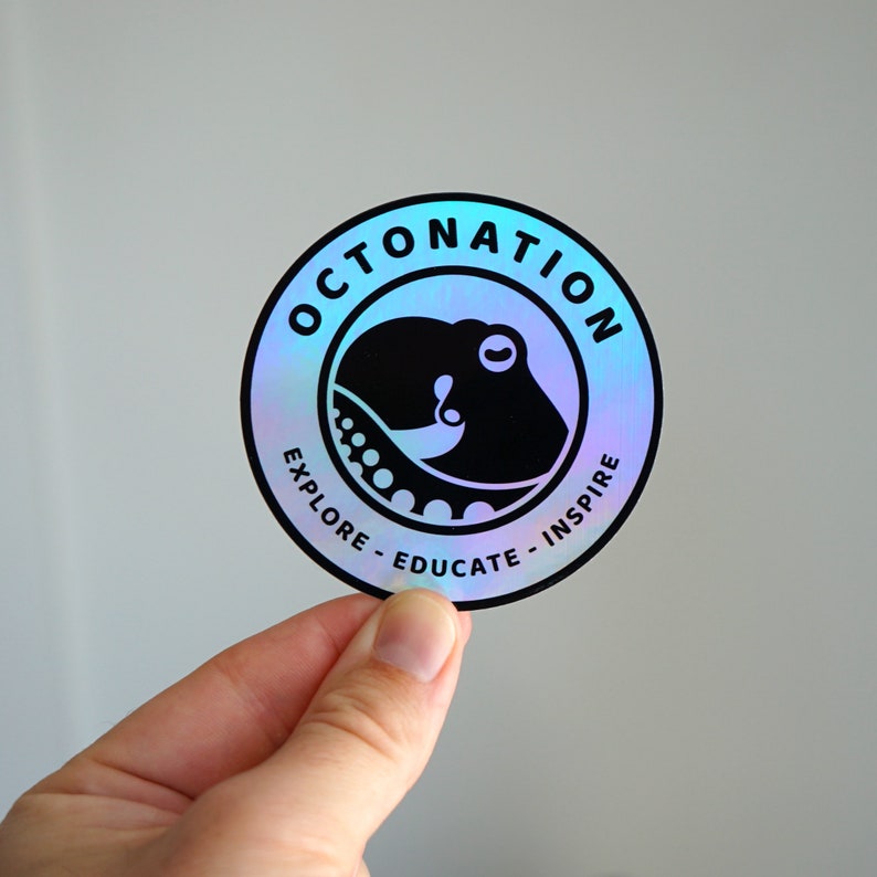 May include: A round, holographic sticker with the text "OCTONATION" in a circle around a black octopus graphic. The sticker also includes the words "EXPLORE - EDUCATE - INSPIRE" in a smaller font.