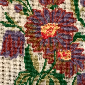May include: Close-up of a floral embroidery design featuring purple, red, and green flowers on a white canvas.
