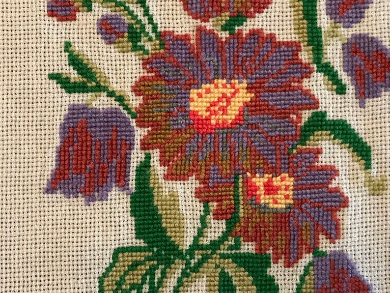 May include: Close-up of a floral embroidery design featuring purple, red, and green flowers on a white canvas.