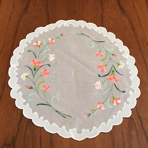May include: A white crocheted doily with a scalloped edge and pink and green embroidered flowers.