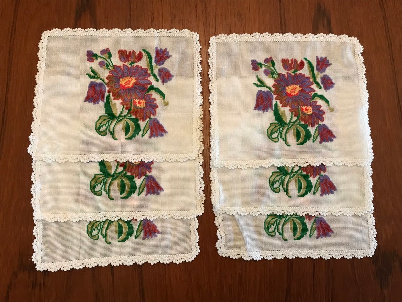 May include: Set of six white crocheted placemats with embroidered floral designs in shades of purple, green, and red.