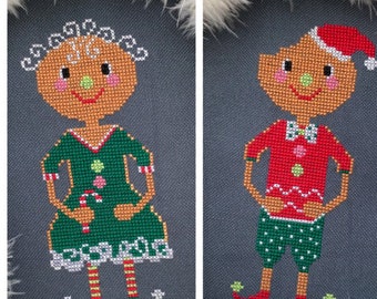 May include: Two cross-stitch Christmas gingerbread figures. One is a gingerbread woman wearing a green dress and holding a candy cane. The other is a gingerbread man in a red shirt and green shorts, wearing a Santa hat.
