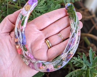 May include: A pink horseshoe with dried flowers and greenery embedded in clear resin.