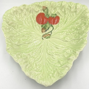 Peut inclure: Un plat de service en céramique vert en forme de feuille de laitue avec deux tomates rouges sur une vigne.