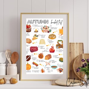 May include: A framed autumn bucket list print with a gold frame. The list includes activities like apple picking, eating candy apples, and visiting a pumpkin patch. The print has a white background with colorful illustrations and the text "Autumn Bucket List".