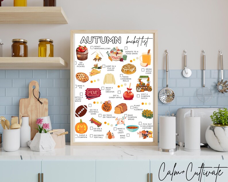 May include: A framed "Autumn Bucket List" print with a light wood frame. The list includes fall activities like apple picking, baking pie, and carving pumpkins. The print is displayed in a kitchen setting with jars and utensils.