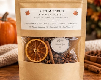 May include: A brown paper pouch containing an Autumn Spice Simmer Pot Kit. The label lists dried orange, cinnamon, cloves, allspice, and star anise. Through the clear window, a dried orange slice, cinnamon stick, and star anise are visible.