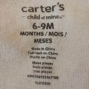 Pode incluir: Close-up de uma etiqueta de tecido branco com o texto "carter's - child of mine" e informa&ccedil;&otilde;es de tamanho para beb&ecirc;s de 6 a 9 meses. A etiqueta tamb&eacute;m inclui o texto "Made in China" e "three pieces".