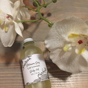 May include: A clear glass bottle with a white label that reads "Nineteen Platinum Dry Wild Watermelon Body Oil 4 fl oz / 120 ml Orchids". The bottle is sitting on a wooden surface with white flowers.
