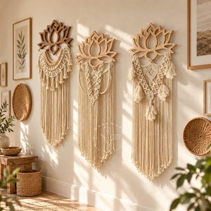 May include: Three wall hangings featuring cream-colored macrame cord knotted into intricate patterns, suspended from wooden lotus flower cutouts. The designs include hanging tassels and fringe, creating a long, textured vertical display on a wall.