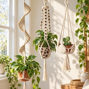 May include: Three off-white macrame plant hangers suspended from hooks. The left hanger features a spiral design with wooden beads. The centre hanger includes dark brown beads and holds a leopard print pot. The right hanger holds a small cactus.