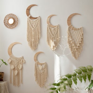 May include: Five macrame wall hangings in the shape of a crescent moon. Each moon is made of natural wood and has a white macrame design with tassels. The macrame is made with cotton cord and has a bohemian style.