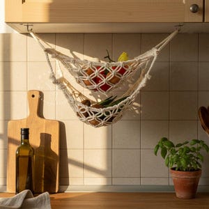 Handmade macramé two-tier fruit hammock in natural cotton, hanging kitchen fruit basket with apples, oranges and kiwis — boho farmhouse decor, space-saving organizer for countertop or wall.